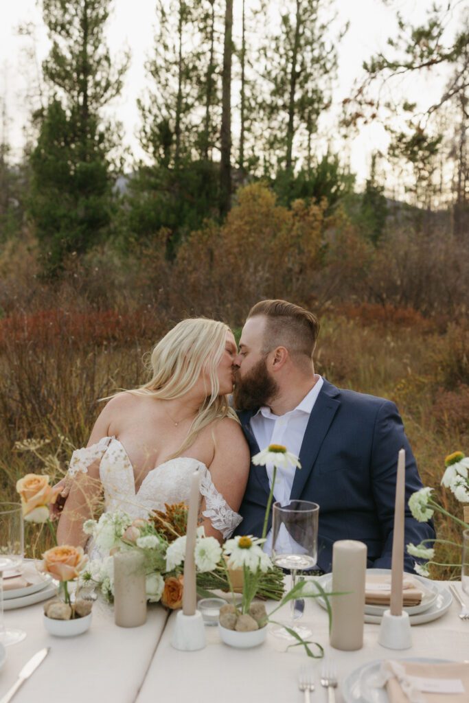 Bailey and Kyle sharing a romantic kiss at their dining table, surrounded by the natural beauty of the Sawtooth Mountains during their elopement