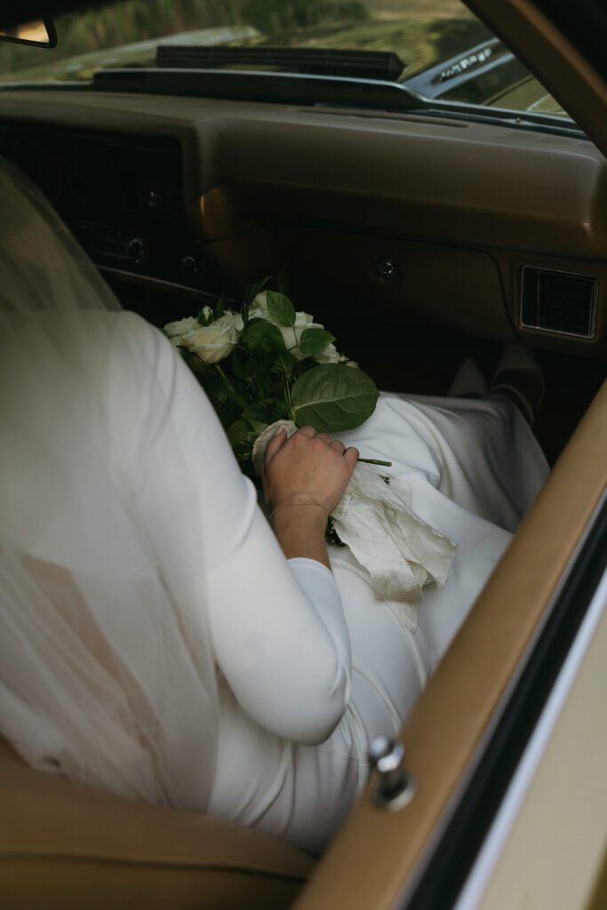 Moriah and Creighton sit together inside their classic car, sharing a quiet, intimate moment on their wedding day