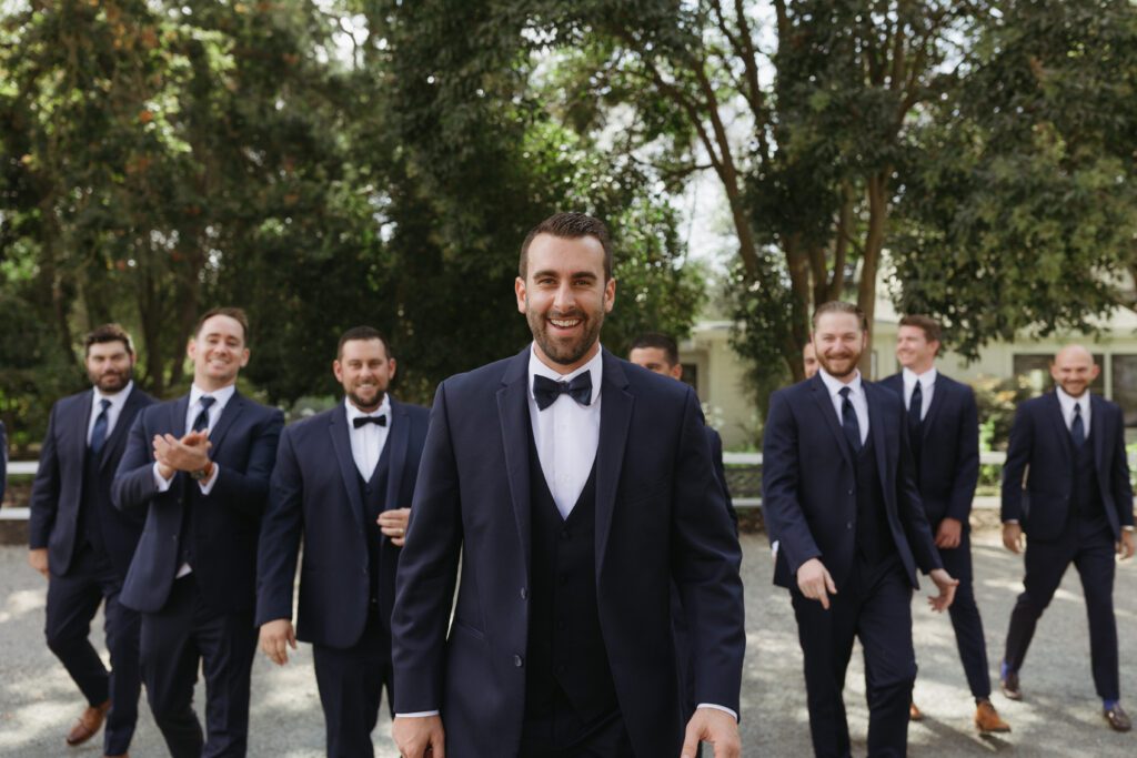 Groom and groomsmen laughing together in a candid moment, dressed in stylish wedding attire