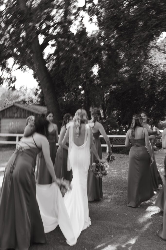 bride walking with her bridesmaids while one helps with carrying the train of her dress