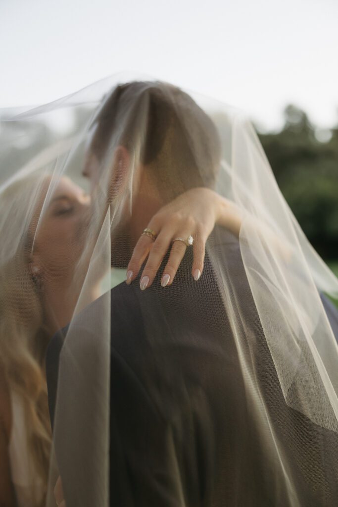 Romantic moment as bride and groom kiss under veil, capturing their love and happiness during their golden hour photos