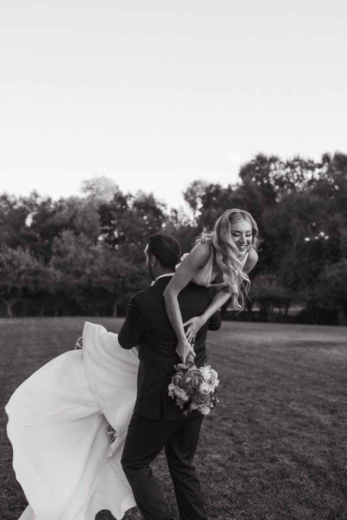 Groom joyfully spinning bride over his shoulder, creating a playful and fun moment during their golden hour photos