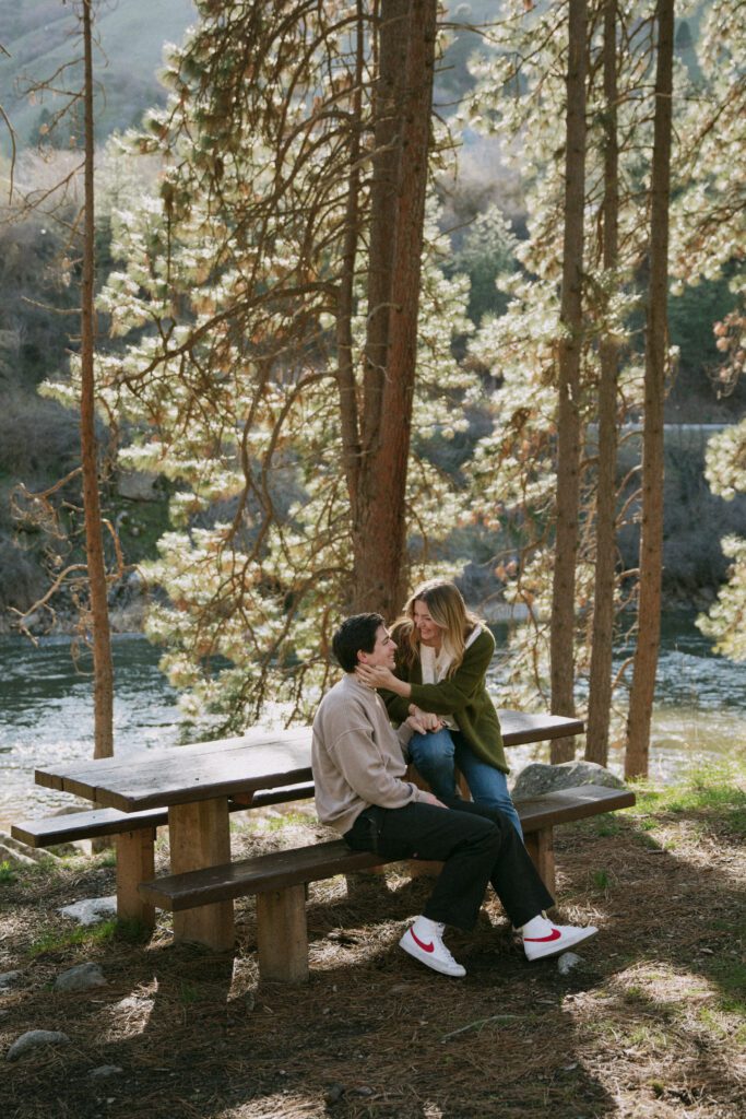 couple sits at picnic table laughing during engagement session in boise.