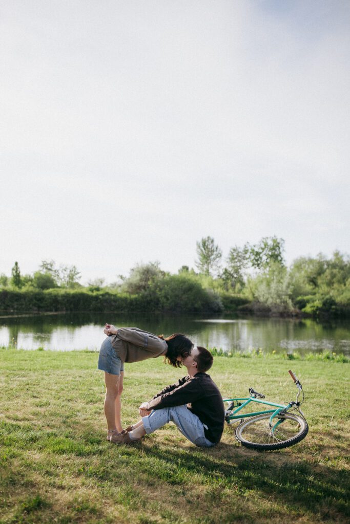 Engaged couple share a kiss as their vintage bike lies beside them, adding charm to the scene.