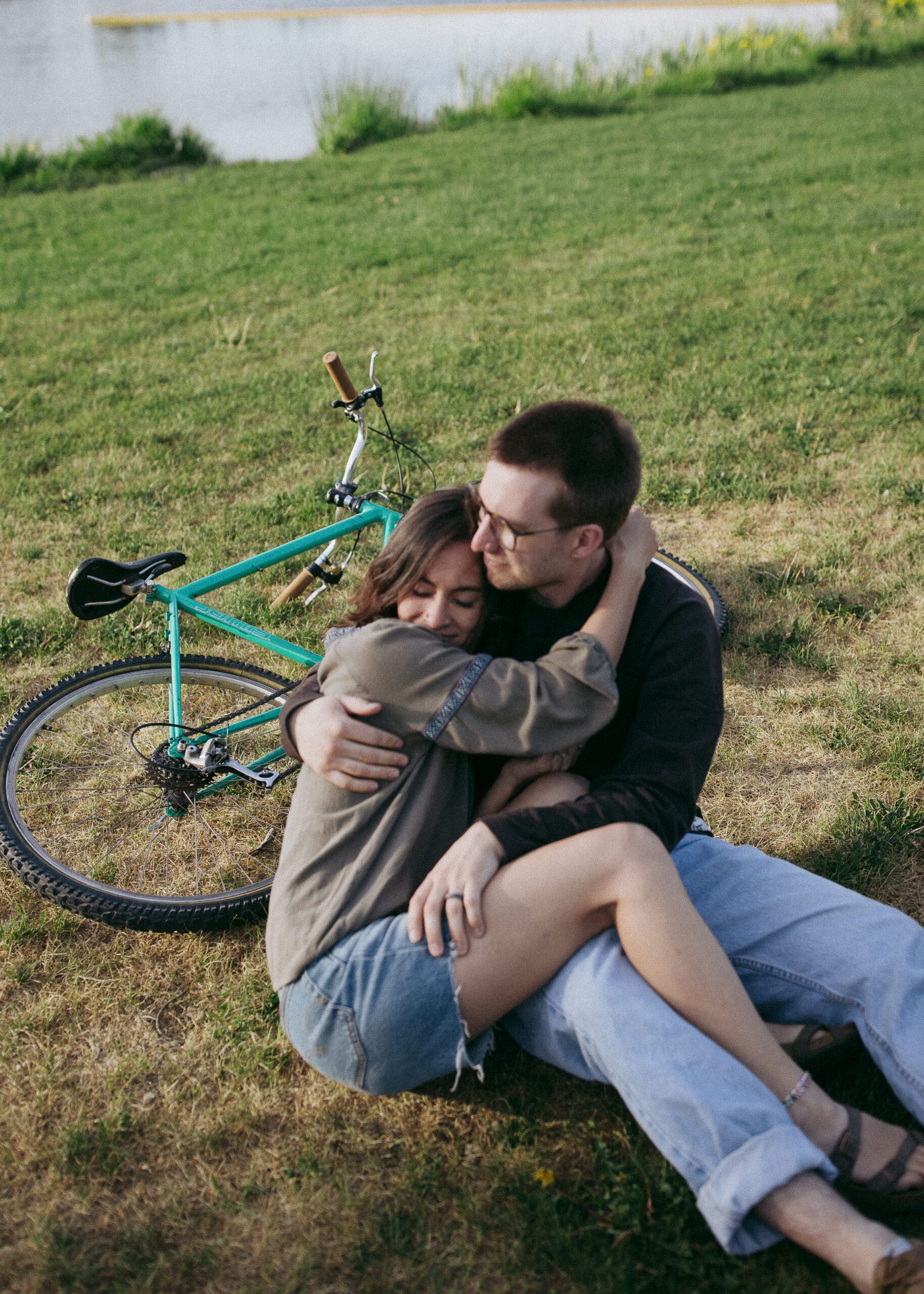 Romantic moment with the couple cuddled up and smiling, framed naturally with their vintage bike in the background.