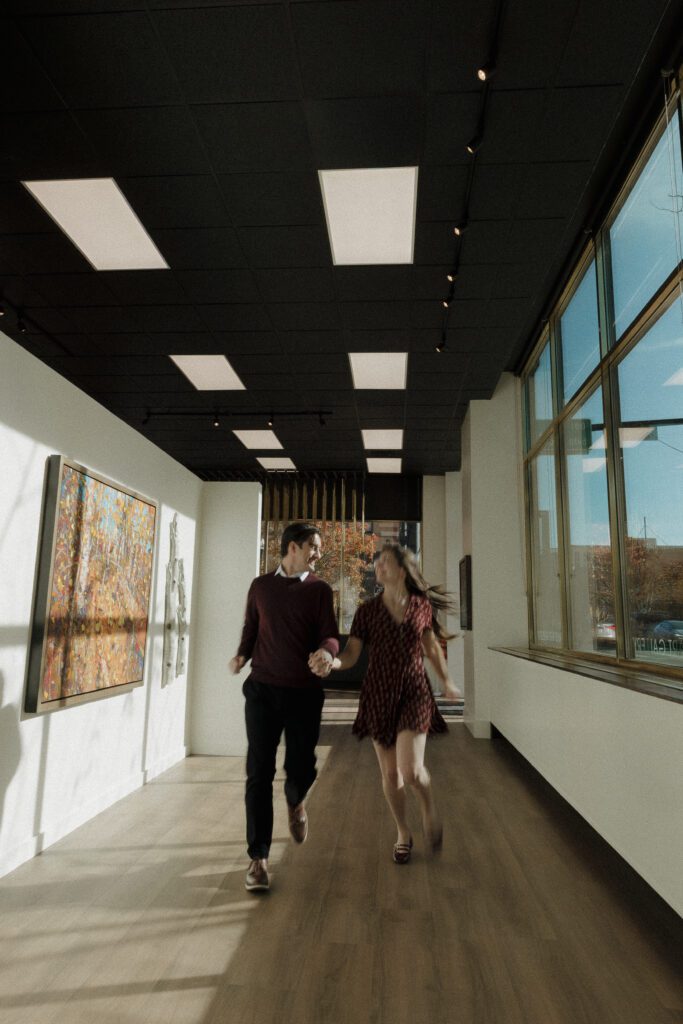 Couple running hand-in-hand down a hallway at local art gallery during their Boise engagement session.