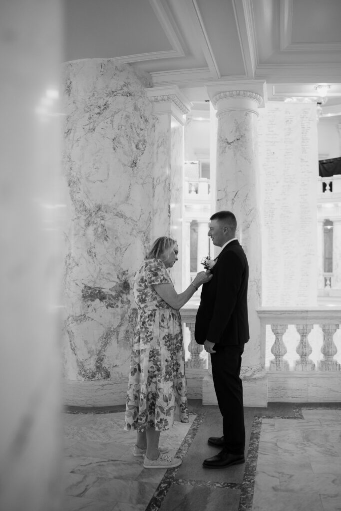 Mother of groom putting boutonniere on his coat before Capitol elopement in Boise.