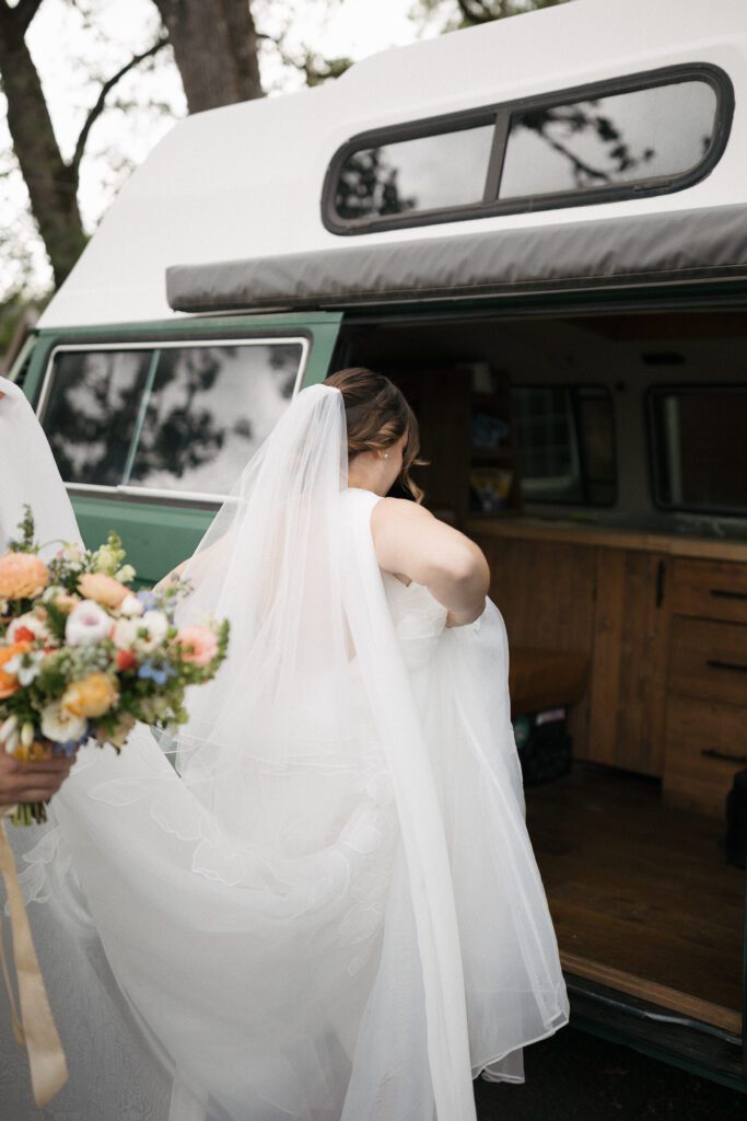 Groom helps bride into travel van during Oregon elopement.