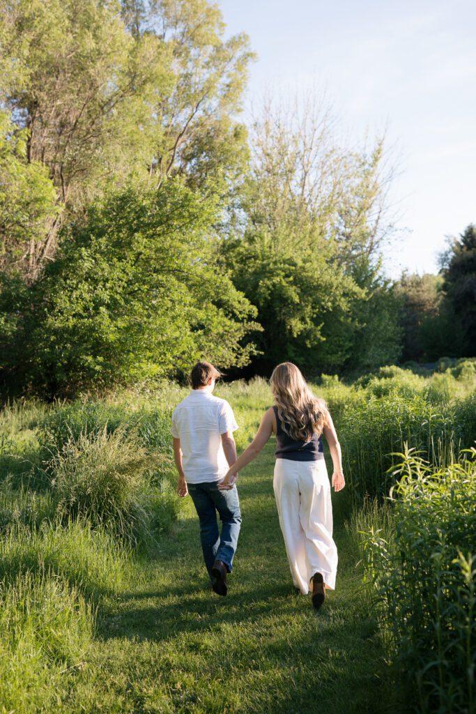 Couple walking hand in hand through a meadow during their Boise engagement session.